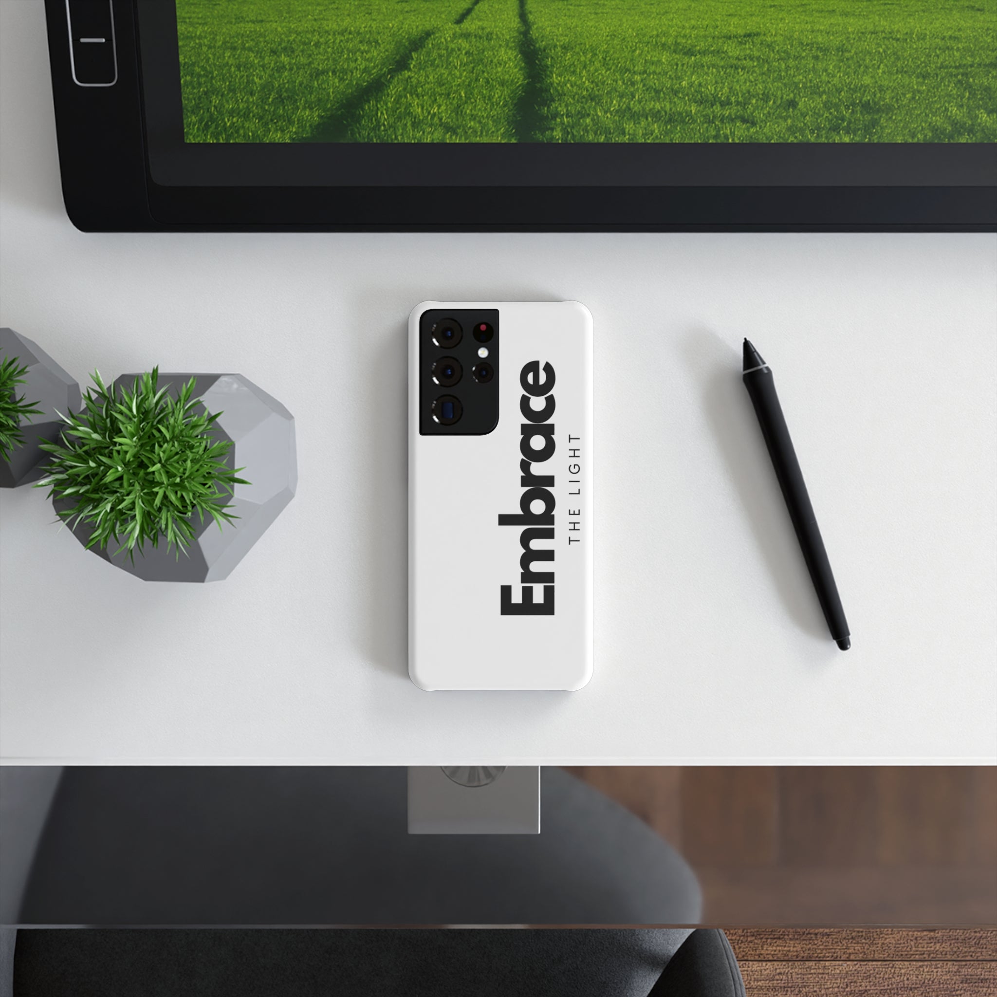 Slim Snap Case on a Samsung phone with 'Embrace the Light' text design, placed on a modern desk with a tablet, pen, and plant. Stylish and protective phone case with a sleek finish.