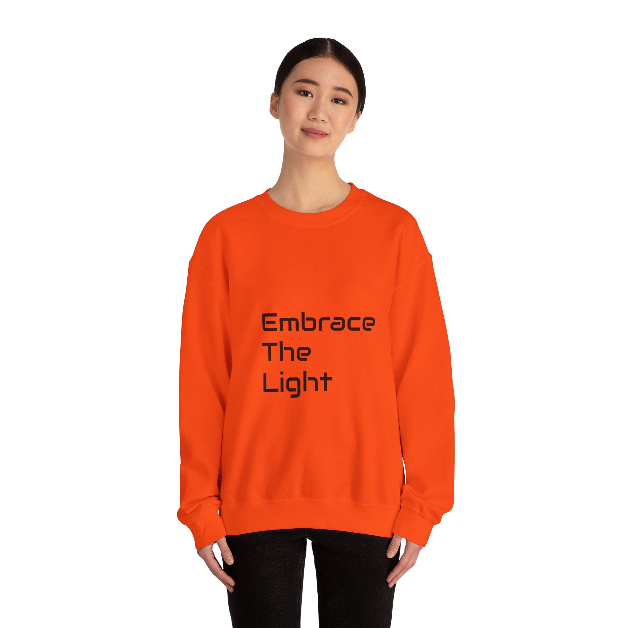 Unisex crewneck sweatshirt in vibrant orange with 'Embrace The Light' text print. Made from a cozy 50/50 cotton blend for comfort and durability.