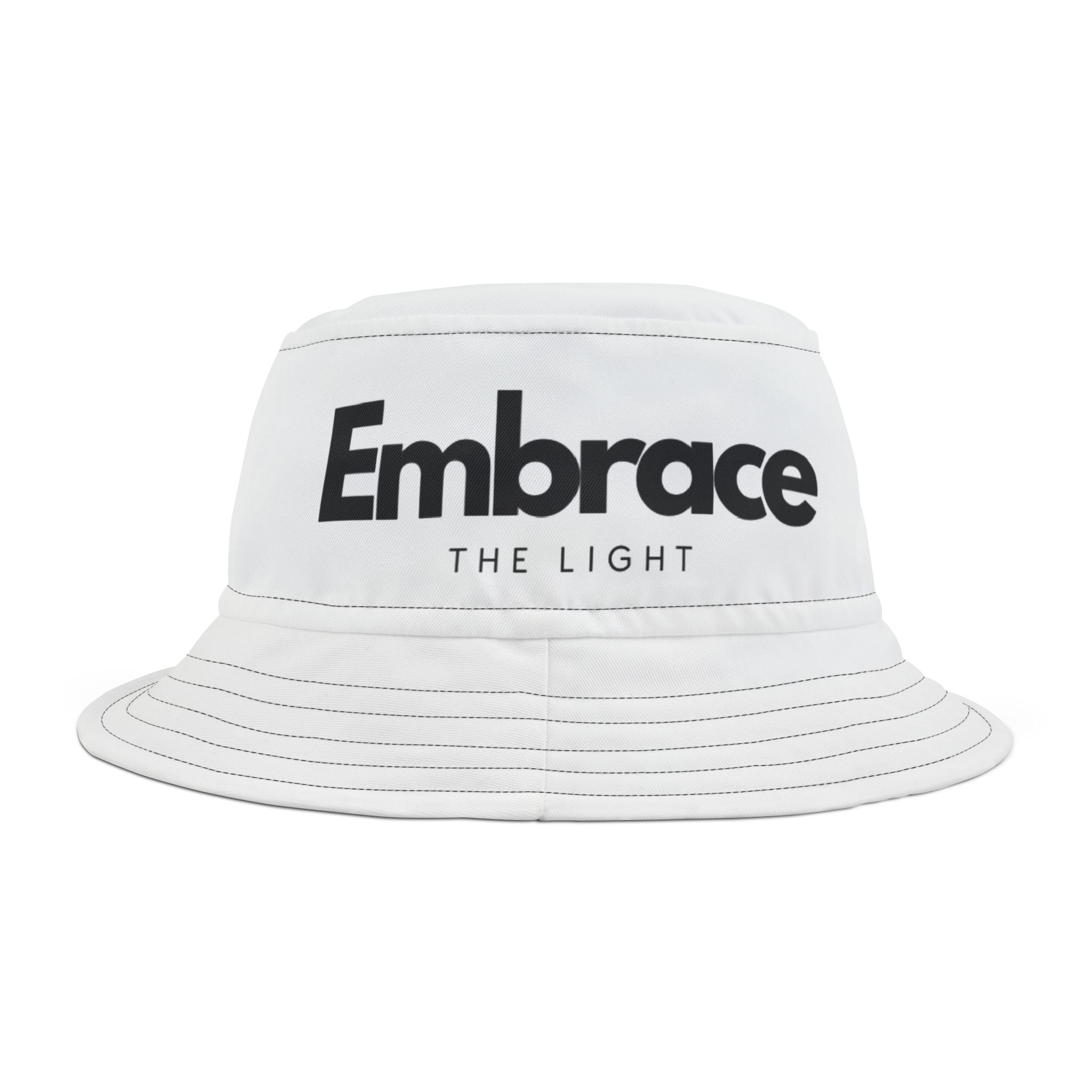 White bucket hat with 'Embrace The Light' text design, made from 100% polyester. Stylish and modern accessory with stitched seam details.